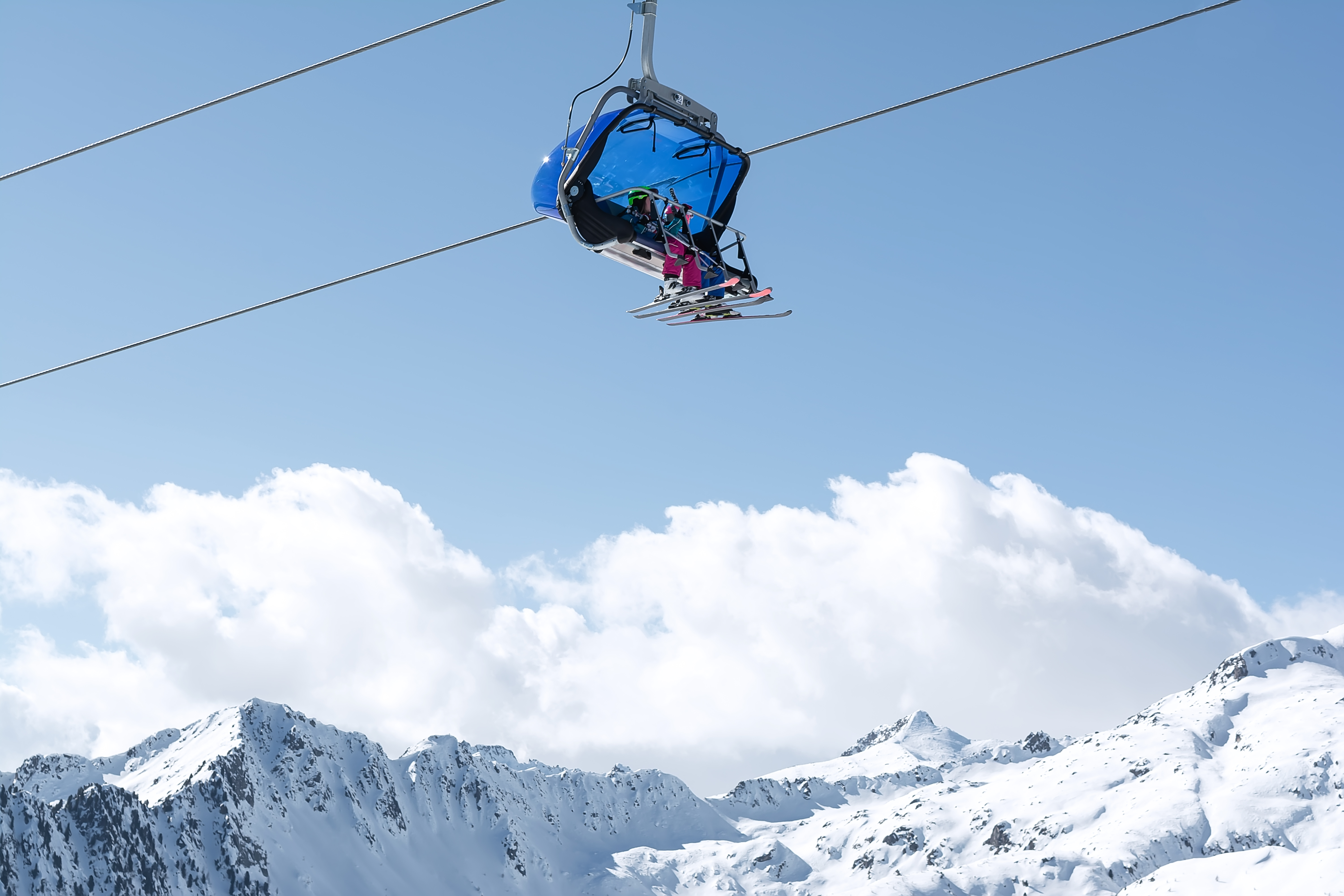 A view of the snow-capped mountains and the cable car with blue chair cabins in which children ride